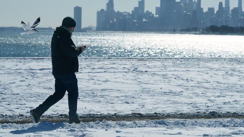 ARCHIVO – Una persona camina cerca de la arena cubierta de nieve en el lago Michigan en...