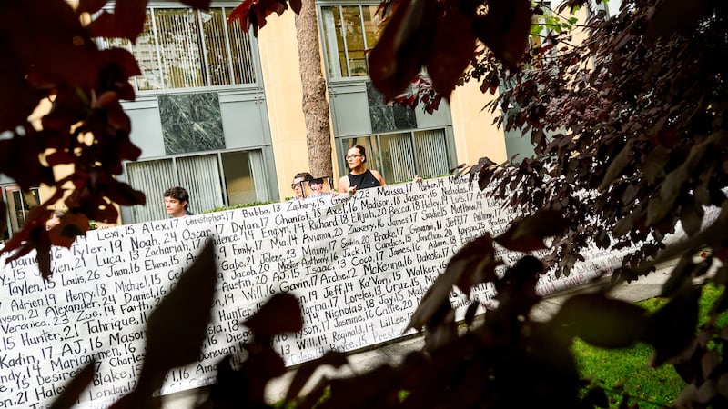 Lennon Torres de Heat Initiative sostiene un cartel con los nombres de jóvenes que, según...