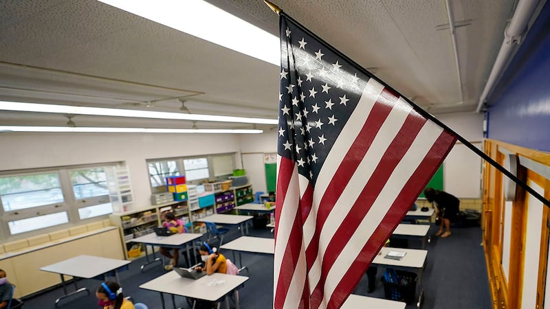 ARCHIVO - Una bandera estadounidense pende en un salón de clases mientras los alumnos trabajan...