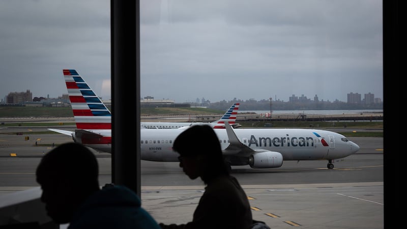 Gente esperando a vuelos mientras un avión de American Airlines circula por la pista en el...