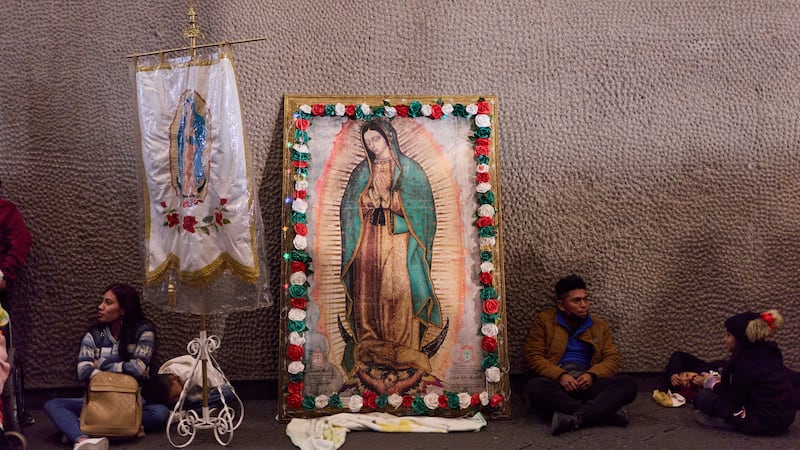 Peregrinos descansan junto a una imagen enmarcada de la Virgen de Guadalupe en el exterior de...