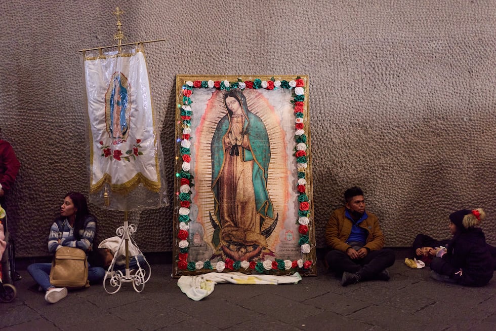 Peregrinos descansan junto a una imagen enmarcada de la Virgen de Guadalupe en el exterior de...